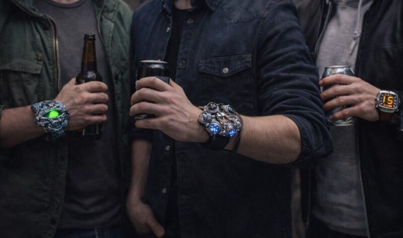 Tri muškarca u ležernoj odeći nose neobične ručne satove različitog dizajna, koji se ističu kao upečatljiv modni detalj u svakodnevnom okruženju