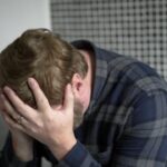 Muškarac sedi u kupatilu i drži glavu zbog bola i nelagodnosti zbog simptoma hemoroida