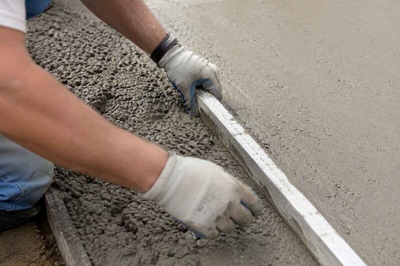 majstor raspoređuje beton po betonskoj stazi uz pomoć drvenog alata u rukama